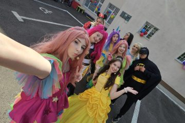 Grup de animatori costumați — prințese, unicorn, Minnie și Batman — pozând pentru selfie, cu baloane în fundal