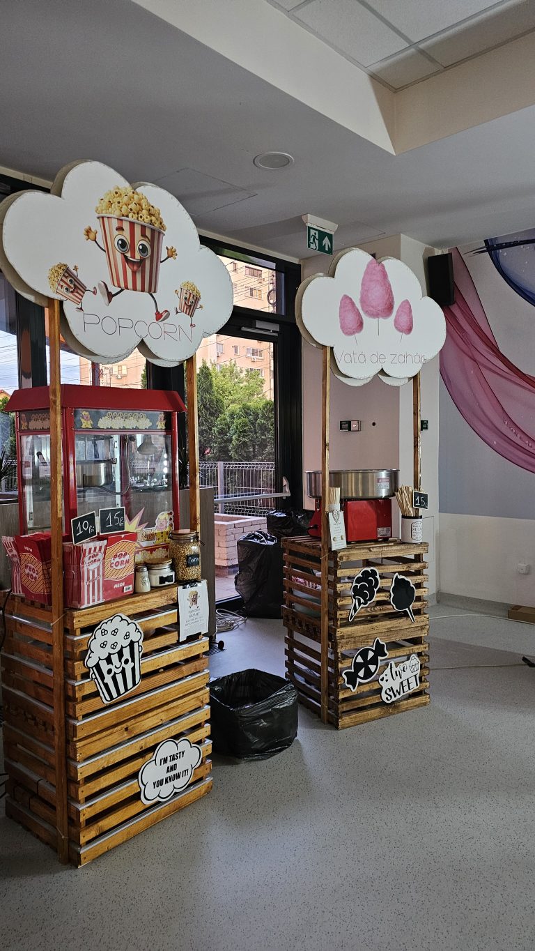 Două standuri pe paleți cu aparat pentru popcorn, aparat pentru vată de zahăr și panouri în formă de nor