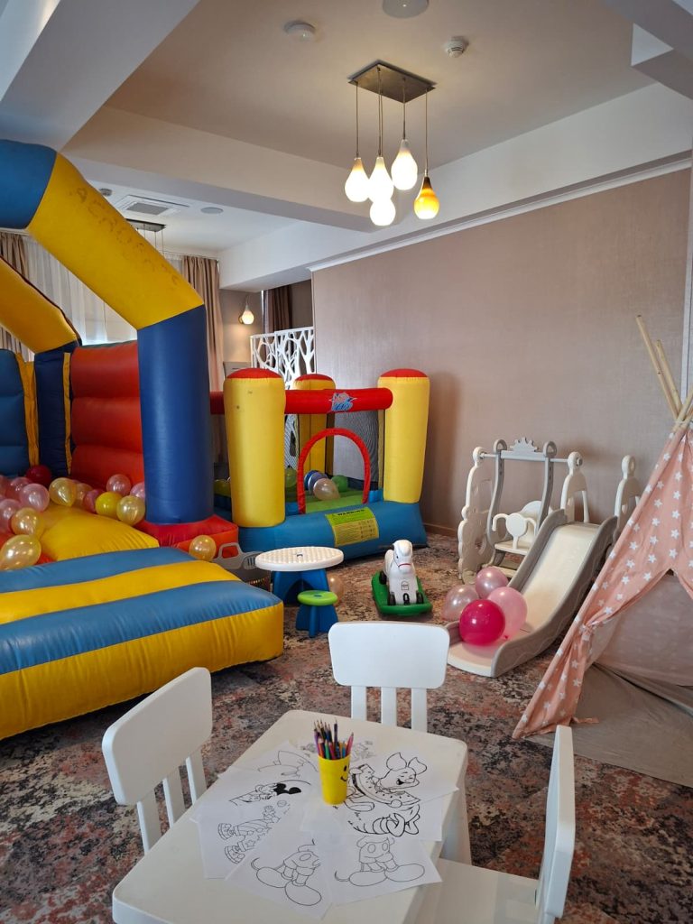 Spațiu de joacă interior cu castel gonflabil colorat, masă de colorat, tobogan și cort teepee