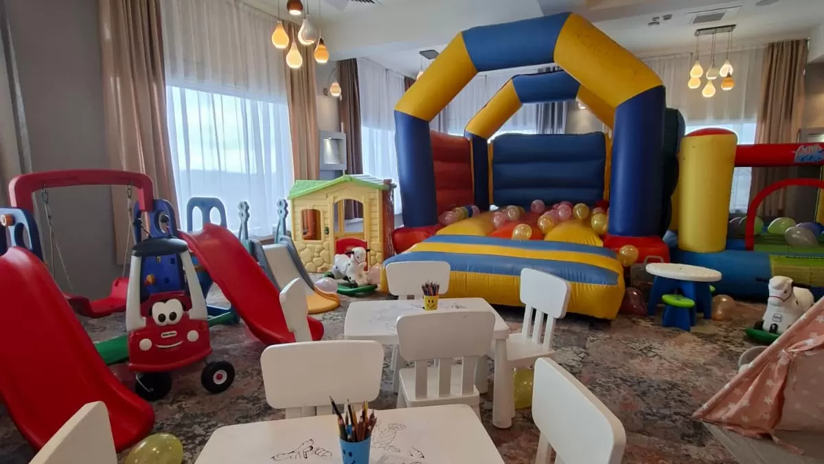 Spațiu interior de joacă cu mese mici, tobogășe, căsuță și castel gonflabil