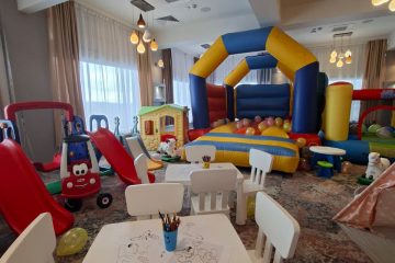 Spațiu interior de joacă cu mese mici, tobogășe, căsuță și castel gonflabil