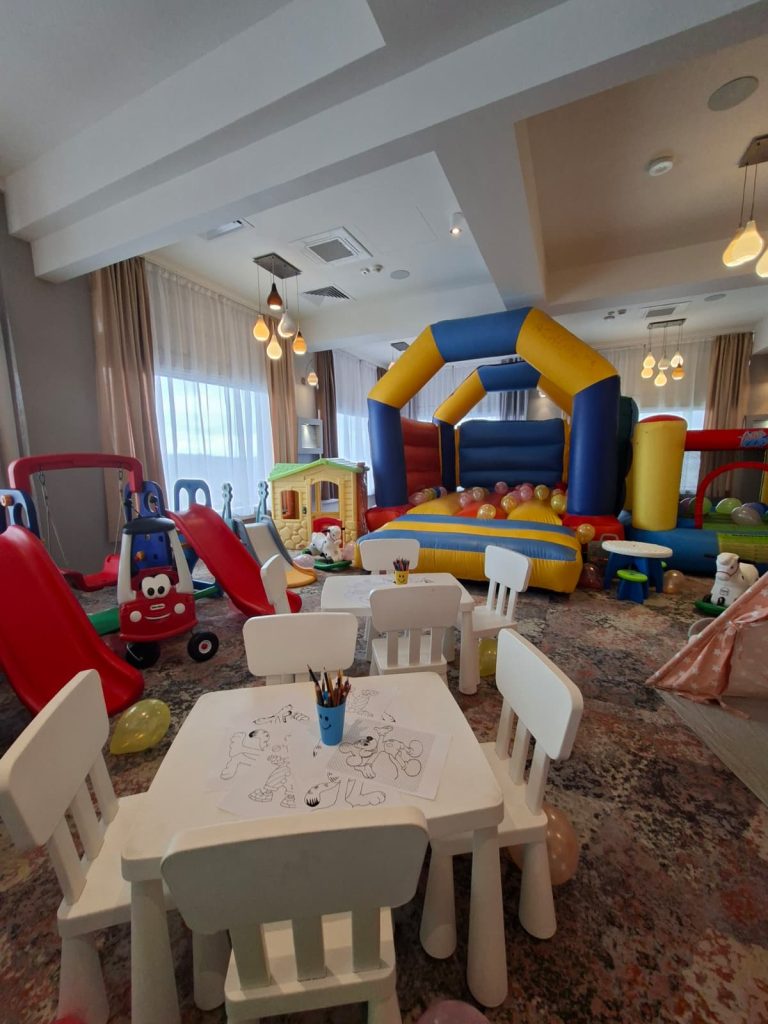 Spațiu interior de joacă cu mese mici, tobogășe, căsuță și castel gonflabil