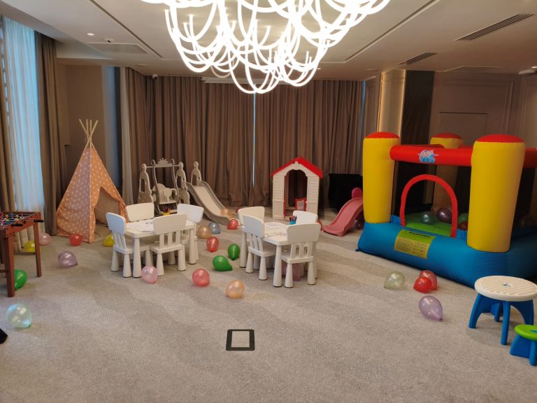 Interior cu colț de joacă: mese de desen, cort teepee, casuță, tobogane și gonflabil colorat