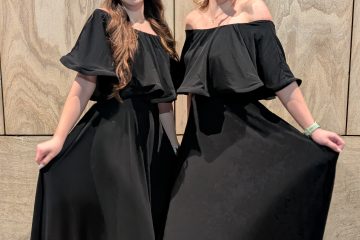 Două femei elegante în rochii negre stând una lângă alta în fața unui perete din piatră