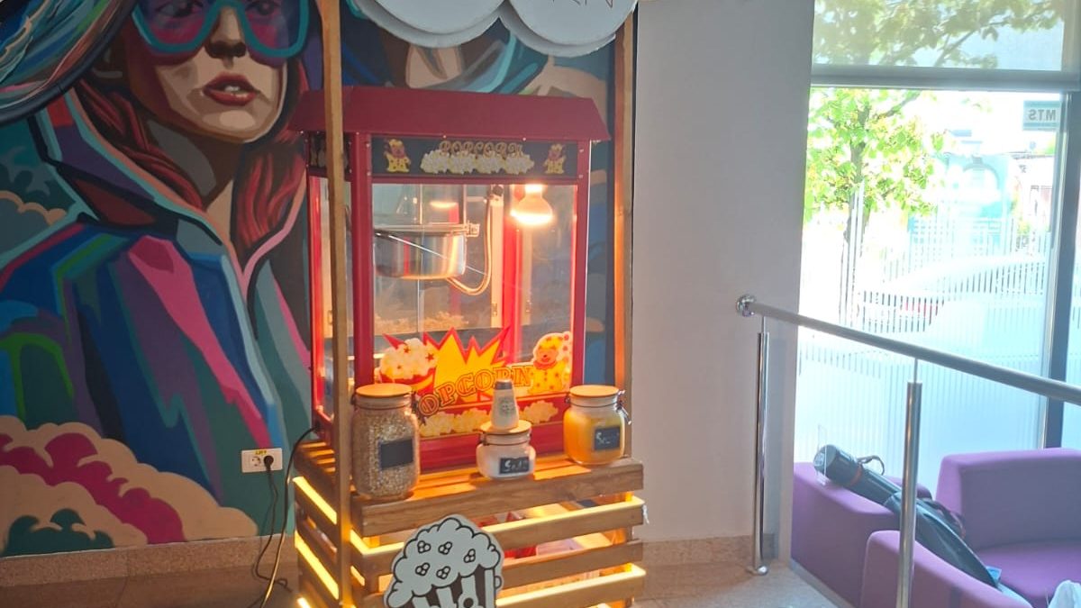 Stand de popcorn iluminat lângă o pictură murală colorată și zone de relaxare.