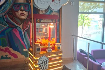 Stand de popcorn iluminat lângă o pictură murală colorată și zone de relaxare.