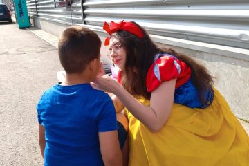 Adult îmbrăcat ca Snow White aplică pictură pe fața unui copil pe scăunel; animatorilor pentru pictură în acțiune, pictură pe față într-un decor outdoor